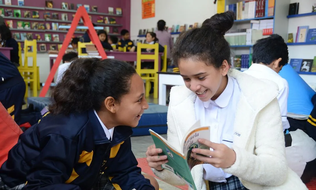 Dos escolares leyendo juntas en una biblioteca escolar